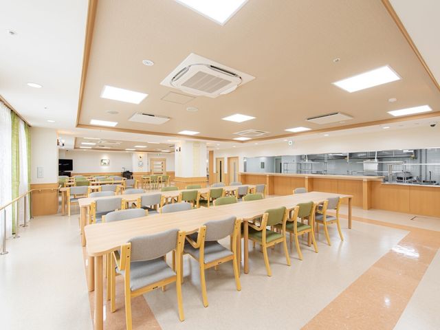 明るいダイニングルーム 食堂 ゆとりあるダイニングで、利用者様が集い食事を楽しむ風景です。キッチンからの新鮮な香りが心地よい空間を演出しています。