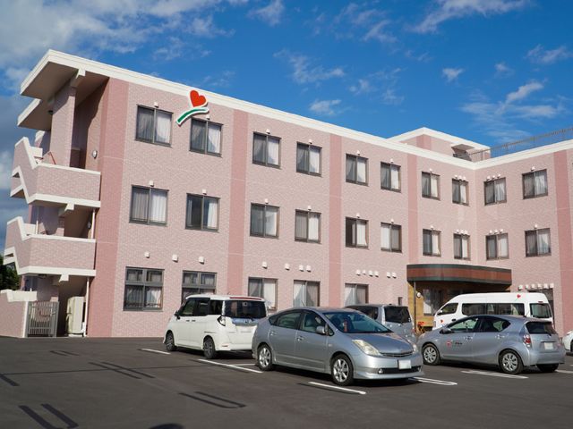 ピンクの外壁の建物 外観 広々とした駐車場があり、アクセスしやすい立地条件の建物です。快適で穏やかな就業環境をお探しの方には最適です。