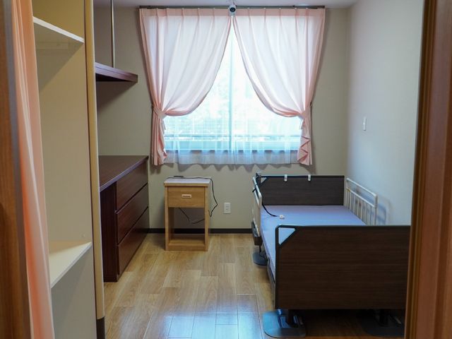 居室のベッドと窓 居室 木目調の家具が落ち着いた雰囲気の居室です。明るい窓辺には、快適な休息を約束するベッドが配されています。