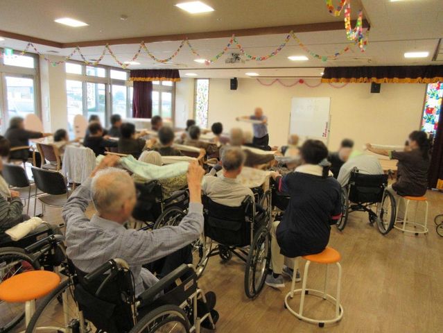 明るい多目的室 多目的室 広々とした空間で、皆がリラックスしながら体操を行っています。自然光が室内を明るく照らしています。