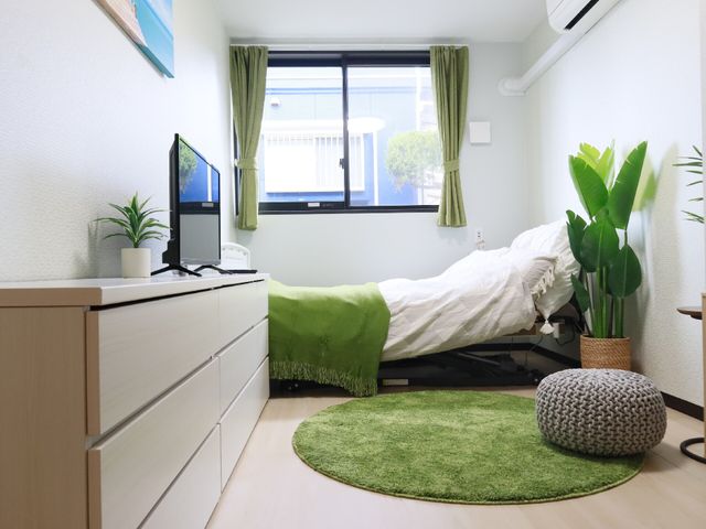 緑のアクセントの居室 居室 清潔感あふれる居室には、ゆったりとしたベッドと緑の植物が心地よい空間を演出しています。快適な作りで、日々の生活が想像できます。