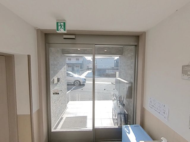 出口から見る外の情景 玄関 明るく清潔感のある出入口からは、穏やかな外の光が差し込んでいます。安全面への配慮が見て取れる設計です。