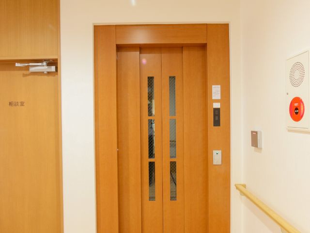 和風の清潔な居室の扉 エレベーター 温かみのある木目調の扉が印象的な居室です。手すりも設置され、安全に配慮された空間が広がっています。