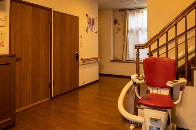 廊下に設置された階段リフト 廊下 手すりと階段リフトが備えられた廊下は、移動のサポートも万全です。木目調の温かみのあるデザインが、訪れる方を心地よく迎えます。