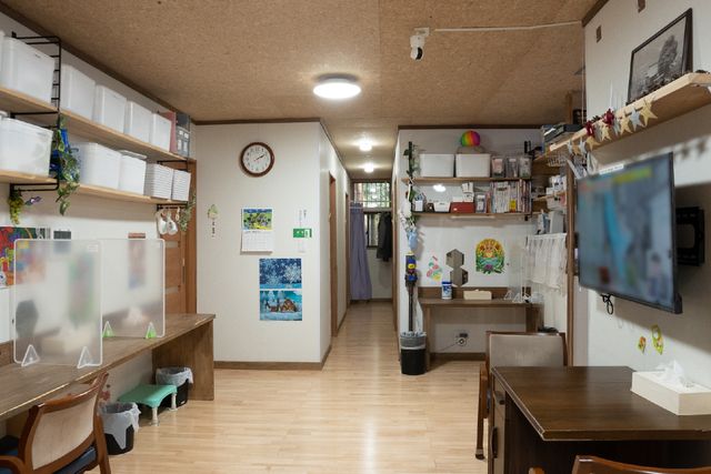 温かみのある廊下の風景 共有スペース ゆったりとした通路には、片側に机や棚が設置され、手作りの飾りが暖かい雰囲気を醸し出しています。壁には時計や掲示物があり、機能的にも配慮された空間です。