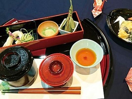 天ぷらやちまき、ふた付きの椀が二つ並び、そばには折り紙で作った鶴が添えられている。