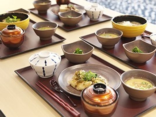 木製のテーブルには和風の料理が並べられた黒いトレーが４組置かれていて、箸が添えられている。