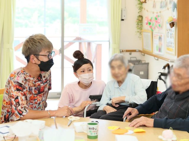 楽しむ様子の居室 居室 広々とした居室で、明るい自然光の中、交流するスタッフと利用者の姿が見られます。