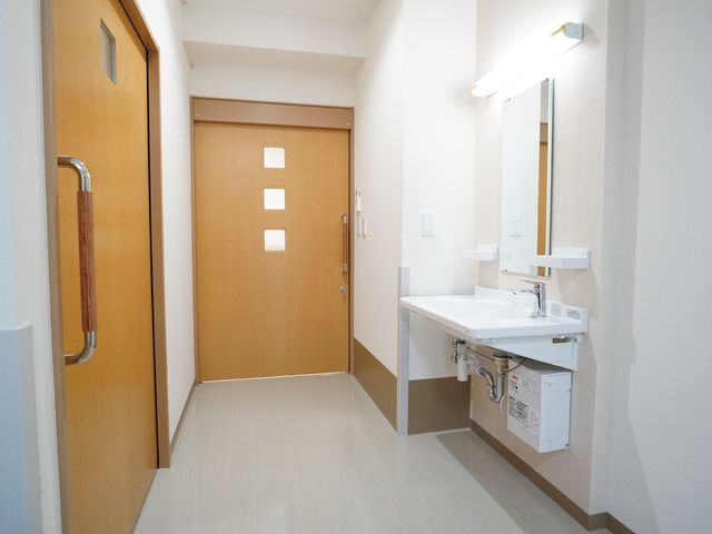 バリアフリー洗面所 廊下 手すりつきの洗面台が設置されており、安全にご利用いただける空間が確保されています。明るく清潔感のある設備は、日々の生活に安心を提供します。