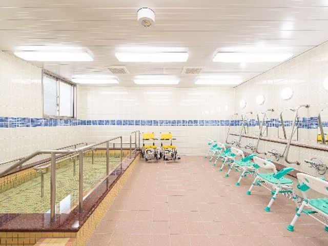 明るく清潔な浴室 大浴場 床には滑りにくい素材を使用し、手すりが設置された快適な空間です。安心して利用できる設計で、利用者さまの快適な生活を支えます。