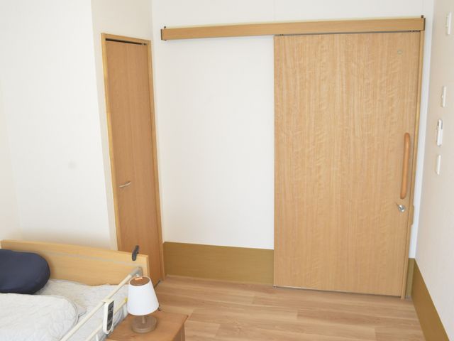 居心地の良い居室 居室 温かみのある木目調でまとめられた居室です。ベッドとサイドテーブルが配置され、落ち着きのある空間を提供しています。