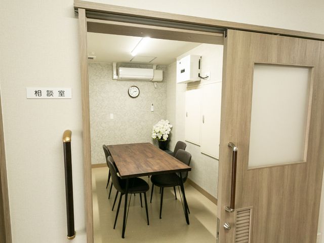 応接室の明るい空間 相談室 広々とした応接室には、テーブルと椅子が整えられ、来訪者を暖かく迎え入れます。清潔感のあるデザインで、居心地の良い待ち合わせ場所となっています。