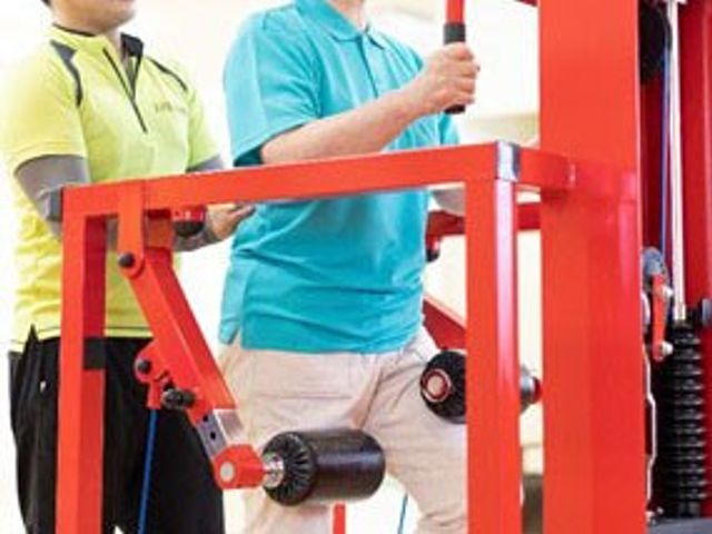 運動中のサポート施設 機能訓練室 スタッフが利用者をサポートしながら、トレーニング機材を使用した運動を行っています。