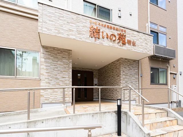 施設の玄関外観 外観   落ち着いた色合いの建物で、玄関まわりは屋根付きです。段差に配慮した手すり付きの通路があり、出入りしやすそうです。