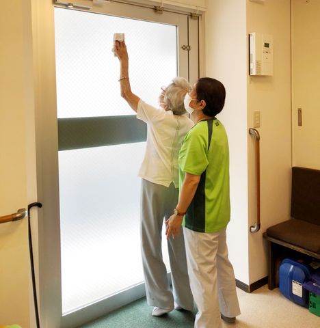 扉の清掃 廊下 明るい廊下で高齢者とスタッフが協力して清掃作業を行い、清潔な環境を保っています。
