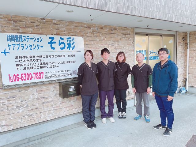 スタッフが立つ看板前 笑顔で立つスタッフたちが、あたたかな印象を与えており、チームワークの良さが伝わります。働く環境の雰囲気が感じられます。