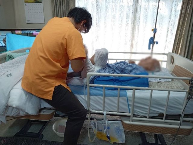 リビングの居室 居室 広々とした居室で、介助者が利用者のケアを行っています。柔らかな自然光が差し込みます。
