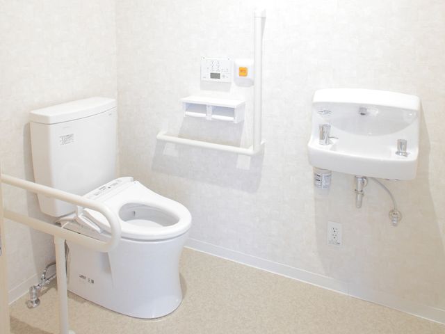 バリアフリー設計のトイレ トイレ 安全かつ快適な使用を支援する手すり付きの明るいトイレです。使い勝手を考慮した洗面設備も整えられています。