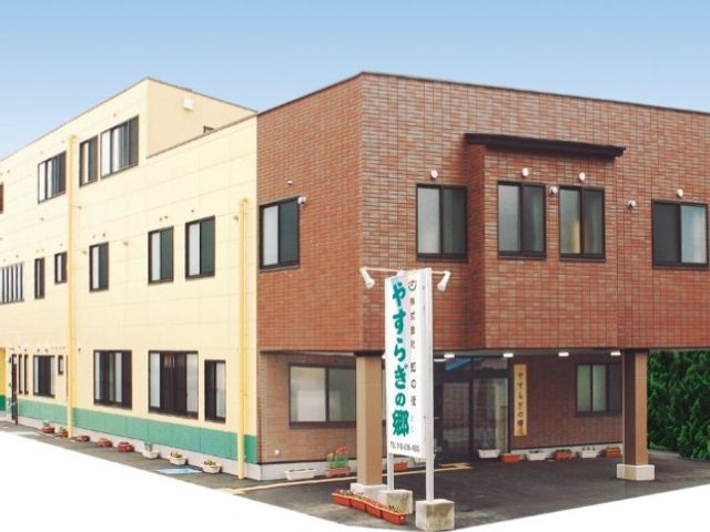 建物外観 外観   落ち着いた色合いの建物で、出入口前には案内の看板が見えます。就業先の雰囲気を外から確認しやすい外観です。