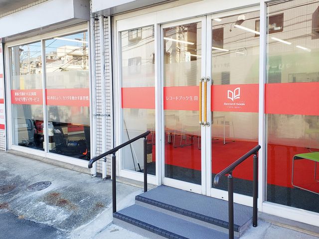 ガラス張りの入口 エントランス   大きなガラス扉と手すり付きの段差が少ない出入口です。明るく入りやすい印象で、通所時の動線が見やすいです。