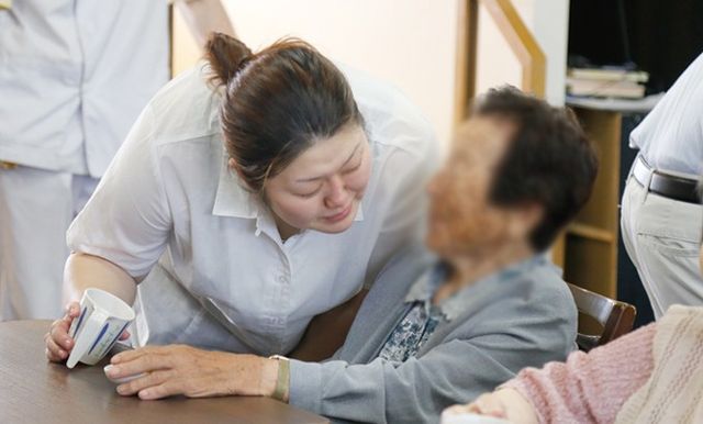 優しいスタッフがいる場所 ダイニングルーム スタッフが入居者に寄り添いながらサポートする様子の場所です。温かい雰囲気を感じられます。