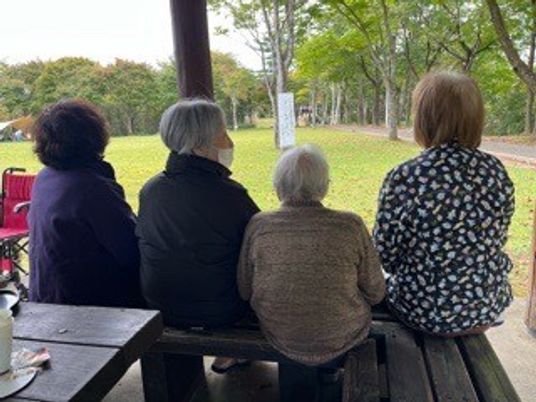 背を向けた高齢者たちが芝生を見守るテラス