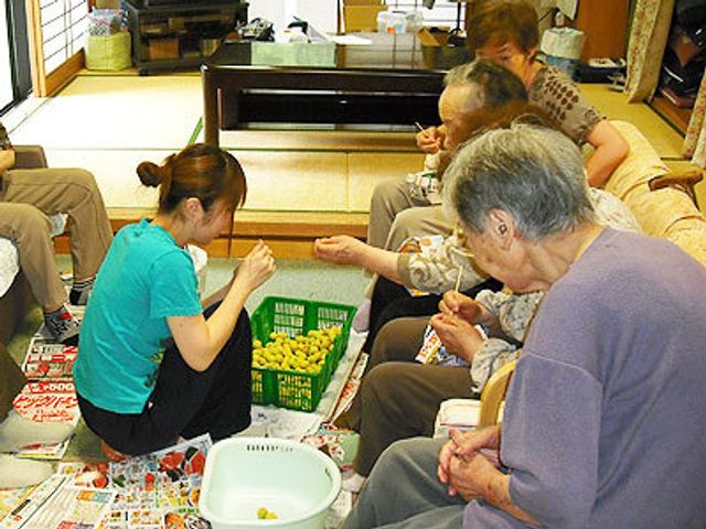 共同での豆さし作業 リハビリ スタッフと利用者が手を取り合い、豆のさし作業に取り組んでいる和やかな場面です。手作業を通じてコミュニケーションを深め、日々の生活に潤いを与えています。