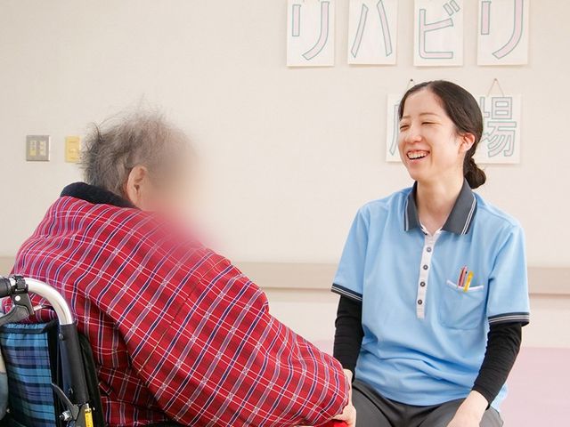 笑顔での会話場面 機能訓練室 広々とした明るい空間で、スタッフが笑顔で入居者とコミュニケーションを取っています。