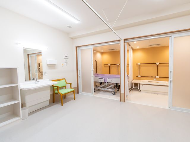 居室の広々とした空間 脱衣所 心地よい居室には、手入れが行き届いたベッドや洗面所があり、利用者の方々の快適な生活を支えています。ゆったりとした作りで、安心して過ごせる空間です。