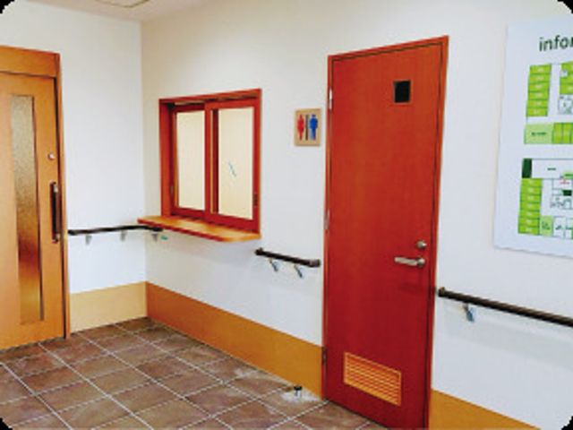 明るい廊下の角 受付 手すりが設置された明るい通路を備え、安全に配慮した作りとなっております。情報掲示板もあり、日々の生活に便利です。