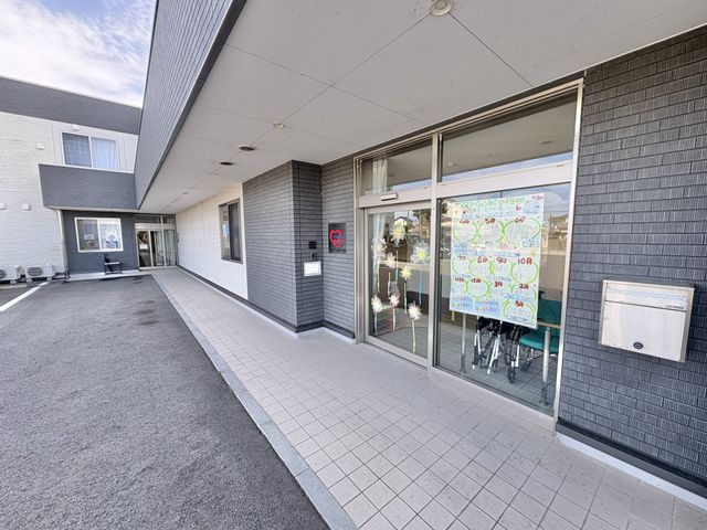 施設の外観と玄関前 外観   明るい庇の下に広いアプローチがあり、出入りしやすそうです。ガラス扉には季節の掲示があり、親しみやすい印象です。