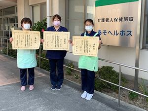 表彰状を持つ職員と看板前  