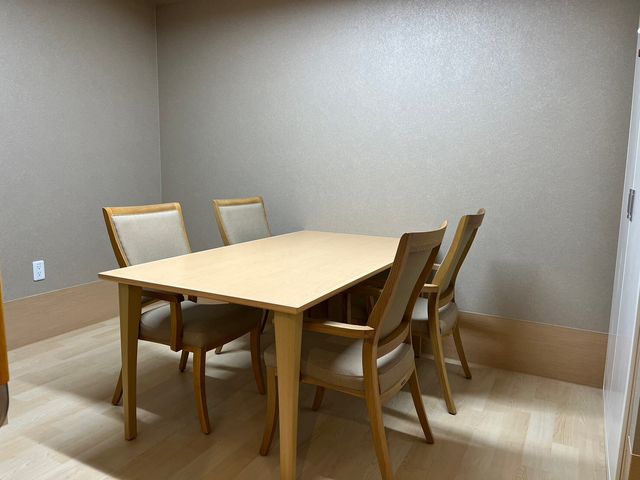 シンプルな居室のテーブルと椅子 相談室 ゆったりとした居室には明るい雰囲気の食事スペースがあり、快適にお過ごしいただけます。明るく落ち着いた色合いで、日々のくつろぎに適しています。