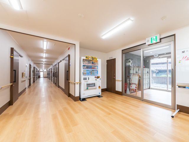 廊下の明るい雰囲気 廊下 広々とした廊下は温かみのある木目調で、手すりも設置されて安全に配慮されています。自動販売機が一角にあり、利用者の方々の小休止にも便利です。