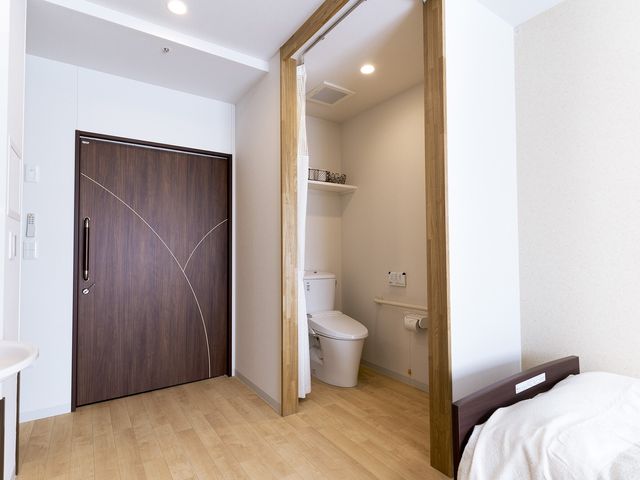 居室のベッドとトイレ 居室トイレ 清潔感あふれる個室で、プライバシーが保たれる快適な空間です。必要な設備が整い、安心して生活できる環境が提供されています。