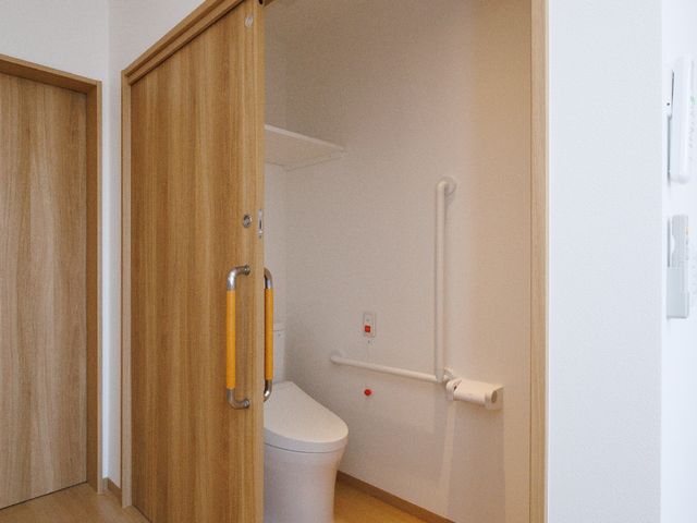 バリアフリー対応のトイレ トイレ 安全に配慮されたトイレスペースは、手すりが設置されており、ご高齢の方でも安心してご利用いただけます。木目調の暖かなデザインが心地よい環境を演出しています。