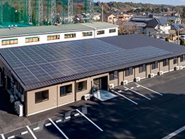 広い駐車場と屋根付き建物 外観 広い駐車場を備えた施設では、車での通勤もスムーズです。屋根には太陽光パネルが設置されています。