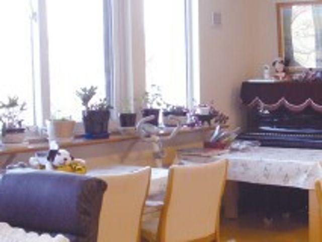 明るいリビングの一角 デイサービス 陽当たり良好なリビングでは、居心地の良い空間でゆったりとした時間を過ごすことができます。窓辺には観葉植物があり、穏やかな雰囲気を演出しています。