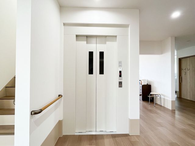 清潔なエレベーター前の廊下 エレベーター 手すりが設置された廊下は広々としており、安全に移動できる構造になっています。エレベーターは待ち時間も少なく、利用しやすい環境です。