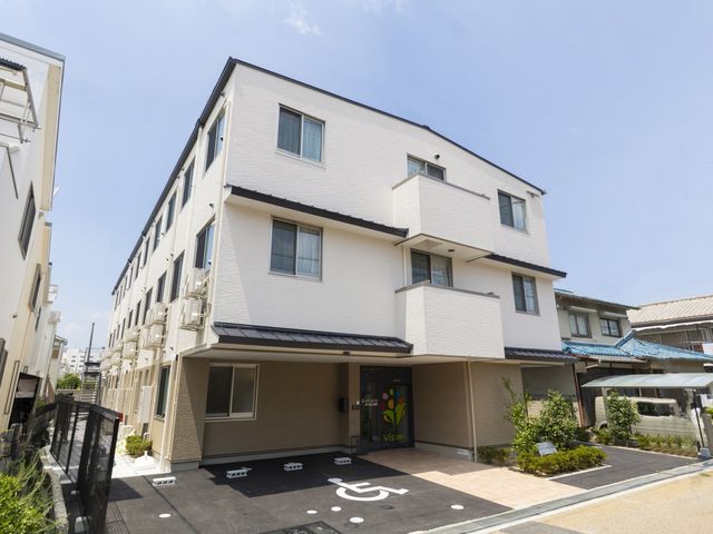 白壁の建物エントランス 外観 明るく清潔感のあるエントランスです。障がいの有無にかかわらず、訪れる皆様が快適に過ごせる環境が整っています。