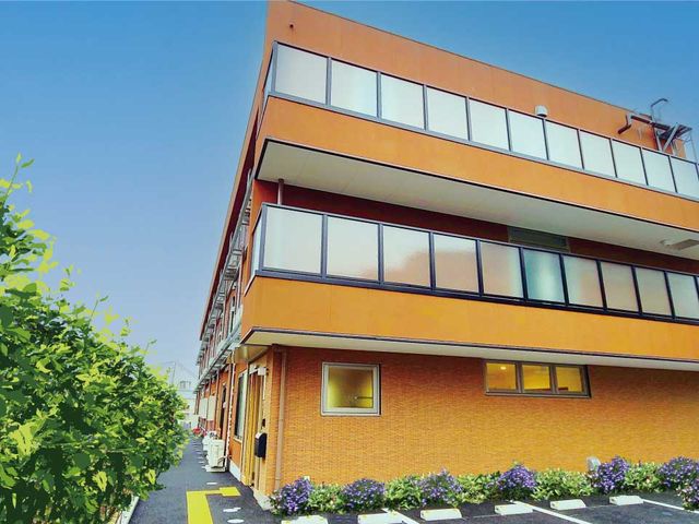 オレンジ色の建物外観 外観 暖かみのあるオレンジ色を基調とした建物です。緑豊かな環境の中で毎日を過ごすことができます。