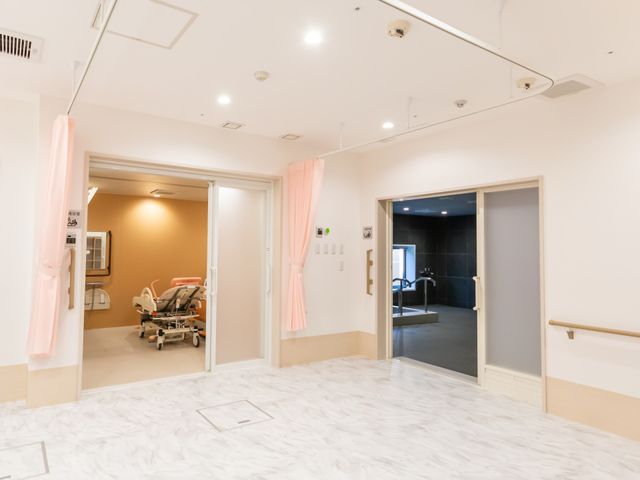 ゆったり廊下と出入口 浴室 広々とした廊下には、移動用のベッドや手すりが設置され、快適な移動をサポートしております。明るく開放感のある出入口が見受けられます。