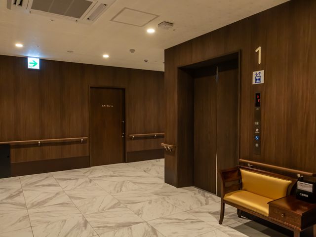 温もりのあるロビー エレベーター 広々としたエントランスには、やわらかい色合いのソファが置かれており、訪れる方を温かく迎えます。適切な高さの手すりも完備され、安全に配慮されています。