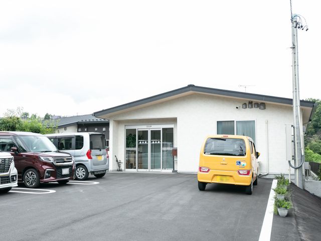 白壁の建物と駐車場 外観 広々とした駐車スペースがあり、入り口までのアクセスが良好です。明るい外観が迎え入れてくれます。