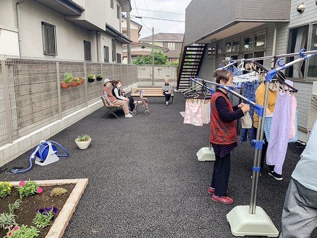 庭で過ごす人々 日常風景 開放的な中庭では、洗濯物を干すなどの日常の一コマを見ることができ、椅子に座って穏やかな時間を過ごす方々の姿もあります。こちらでの仕事は、日々の豊かな生活を支えるやりがいを感じられるでしょう。