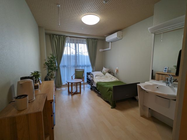 ゆったり居室の一例写し 居室 使い勝手を考慮した落ち着いた雰囲気の居室です。手入れが行き届いた緑や設備の様子が見受けられ、快適な生活空間が提供されています。