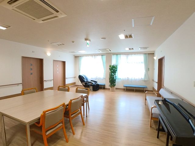 多目的利用可能な居室 共有スペース 広々として清潔感のある居室は、窓から自然光が差し込み、明るい雰囲気を演出しています。複数のテーブルと椅子が配置され、様々な活動に使用できるスペースです。