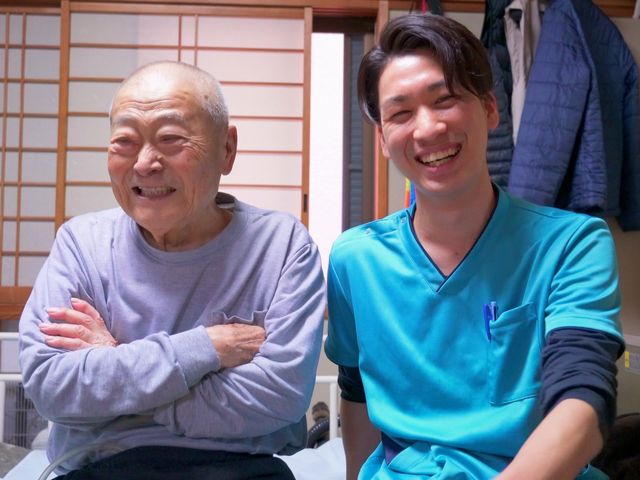 笑顔の利用者とスタッフ 温かな対話が交わされる居室で、利用者とスタッフが笑顔でコミュニケーションをとっています。働く環境の一端を垣間見ることができます。