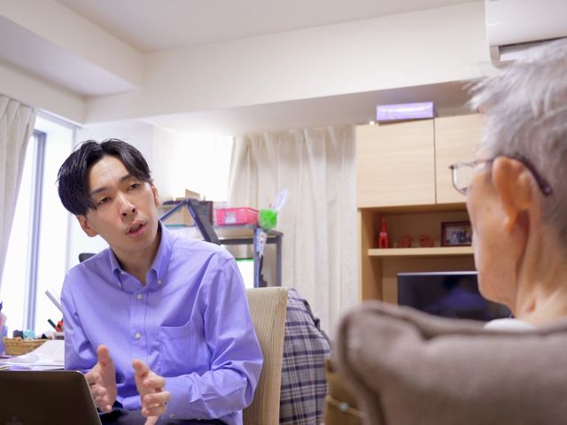 スタッフと利用者の対話 スタッフが利用者の方と向き合って、丁寧に対話を交わしている居室の風景です。コミュニケーションを大切にする温かな雰囲気が感じられます。