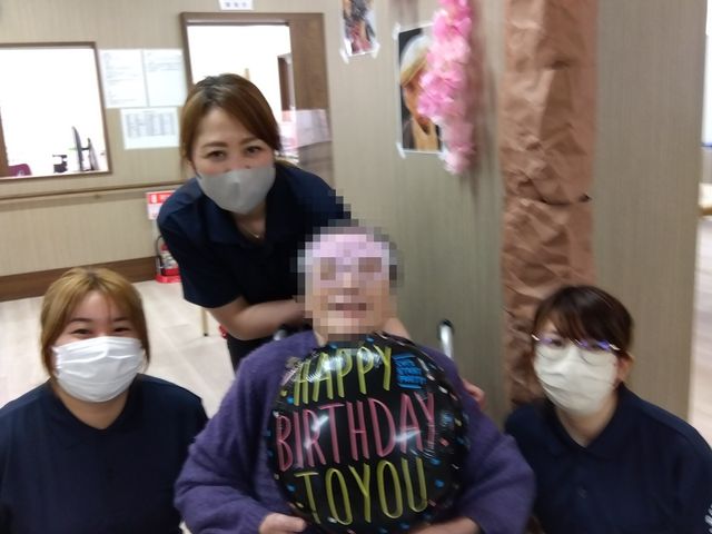 お祝いの様子の廊下 スタッフと入居者様 笑顔あふれるスタッフに囲まれた心温まる瞬間です。温かみのある環境での業務を望む方にとって、理想的な職場かもしれません。